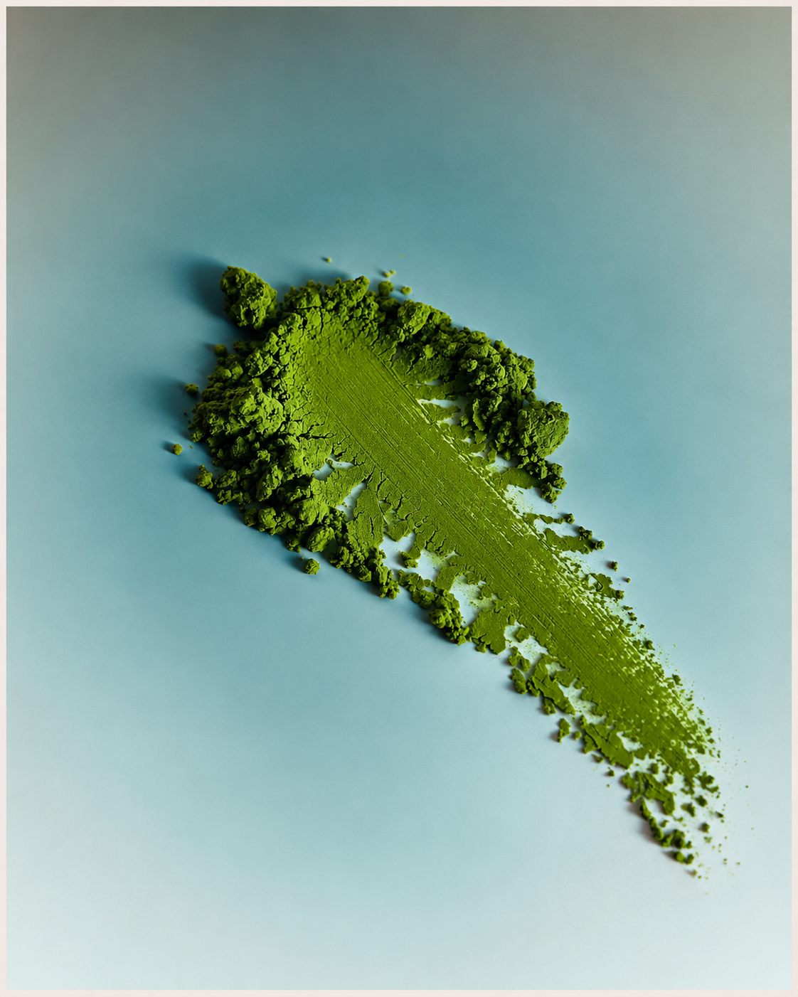 Swoosh of loose matcha green tea powder on a light blue surface, overhead shot